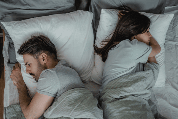 Top-down view of a couple sleeping in bed, man on the left and woman on the right under grey blankets.