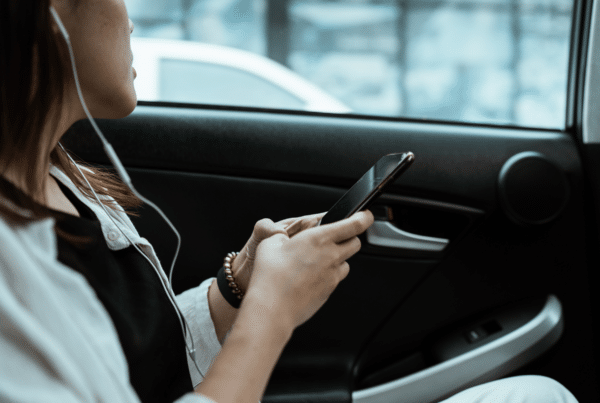 Person in a car using a smartphone with wired earphones plugged in, resting on a door panel edge.