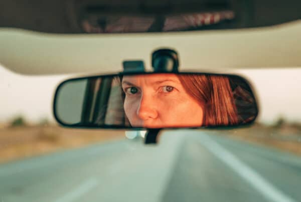 Close-up of a driver's eyes reflected in a car's rearview mirror, with red hair visible to the side.